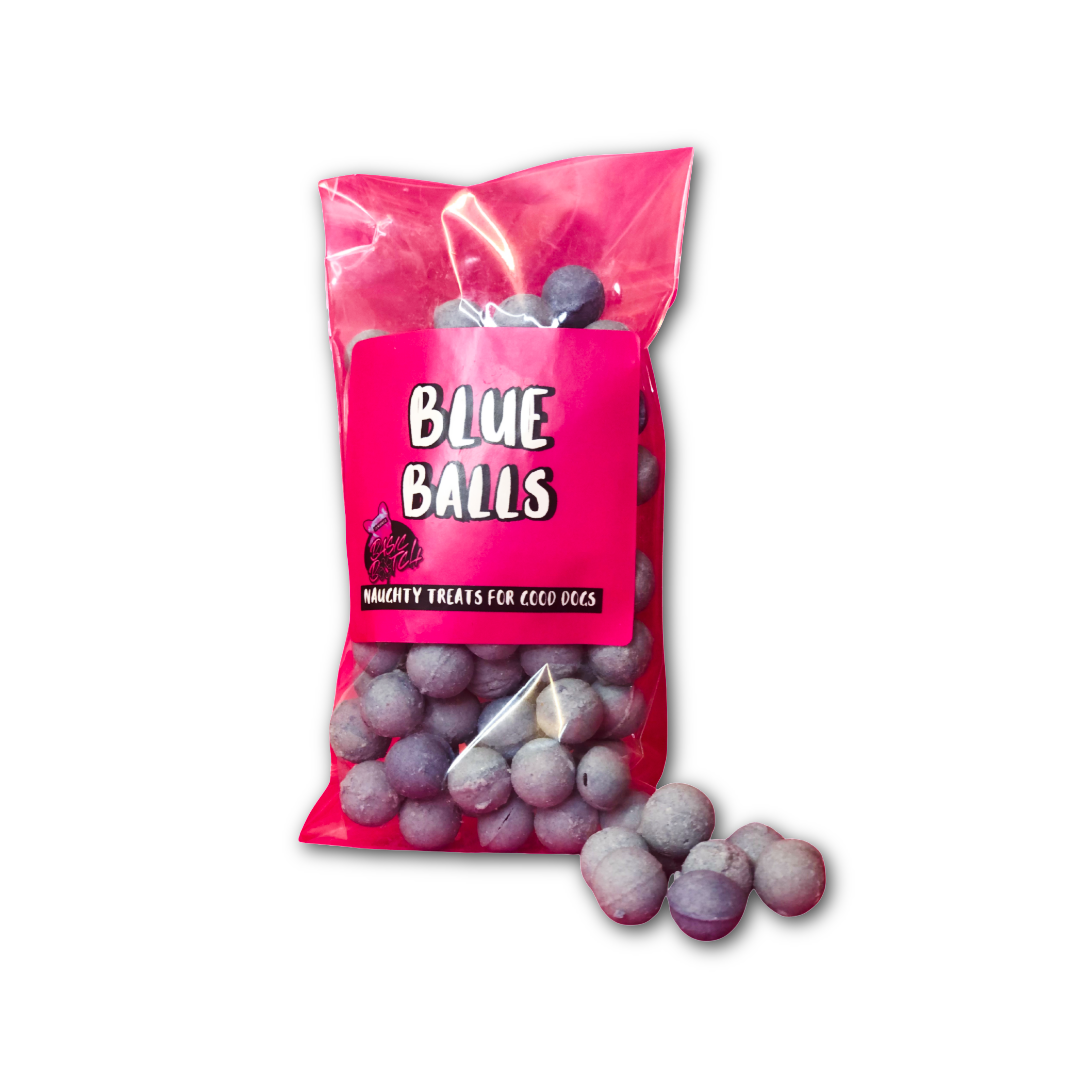 Packet of small blue dog chocolate balls, with 'Blue Balls' in white writing on a pink sticker. A small selection of blue balls are out of the packet. On a white background.