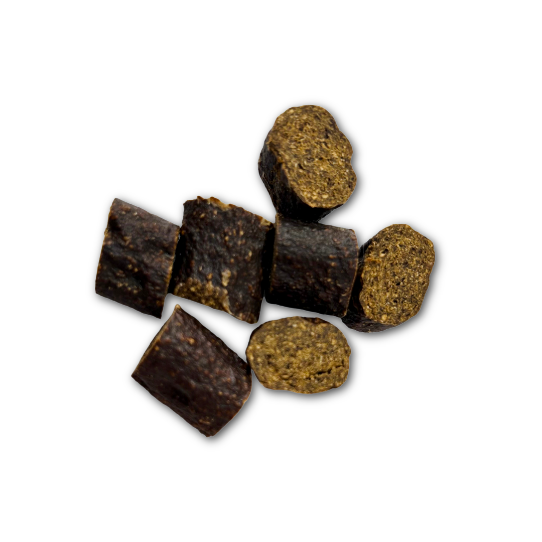 7 pieces of dark brownish-black chopped sausage dog treats on a white background.