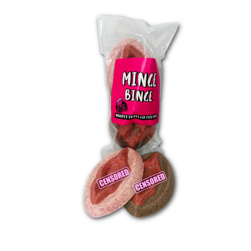 Packaged dog treats in the shape of cartoon pink and brown female flower chocolates with 'Minge Binge' in white writing on a pink sticker. One pink and one white female flower chocolate outside of the packet. On a white background.